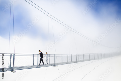 Girl and boy walking on bridge in clouds