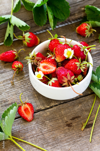 Fresh strawberries in a bowl on a wooden rustic table.