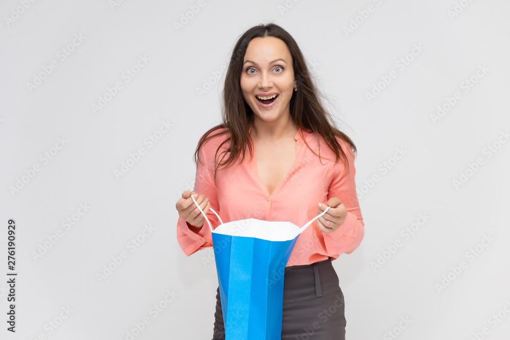 Portrait to the waist of a young pretty brunette woman of 30 years in business clothes with beautiful dark hair with a blue shopping bag. On a white background, talking, showing hands, with emotions Portrait to the waist of a young pretty brunette woman of 30 years in business clothes with beautiful dark hair with a blue shopping bag. On a white background, talking, showing hands, with emotions