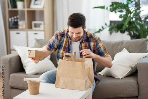 consumption, eating and people concept - smiling man unpacking takeaway food at home photo