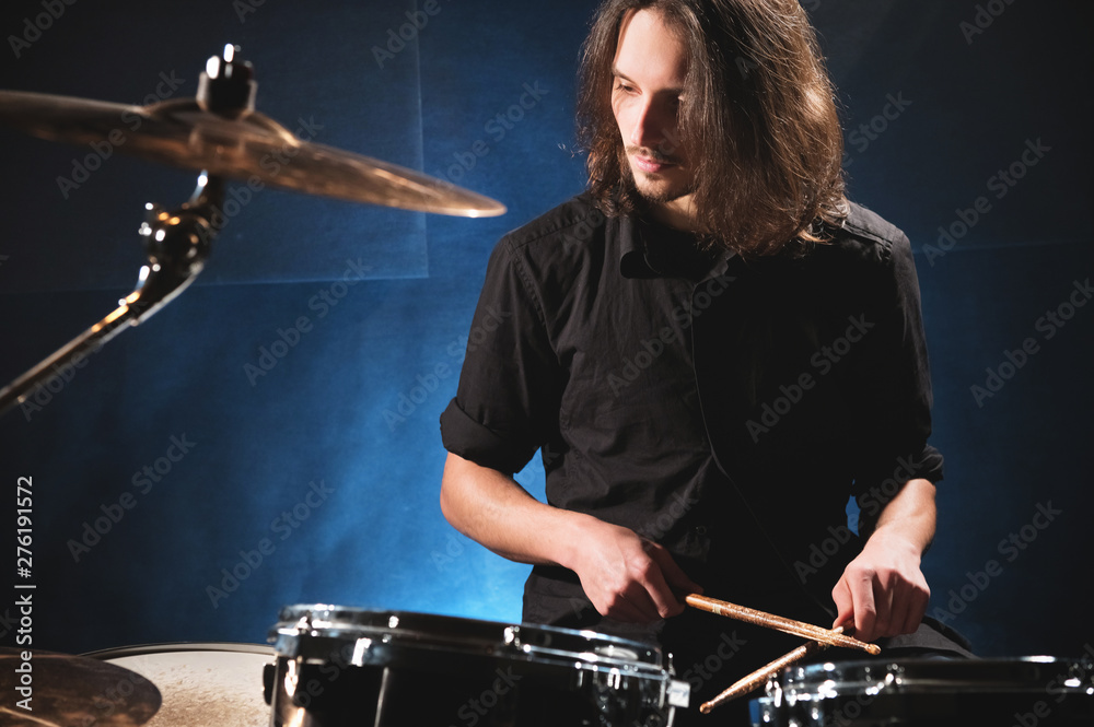 Fototapeta premium Portrait of a long-haired drummer with chopsticks in his hands sitting behind a drum set. Low key. Concepts of the creative freedom of the millenial generation