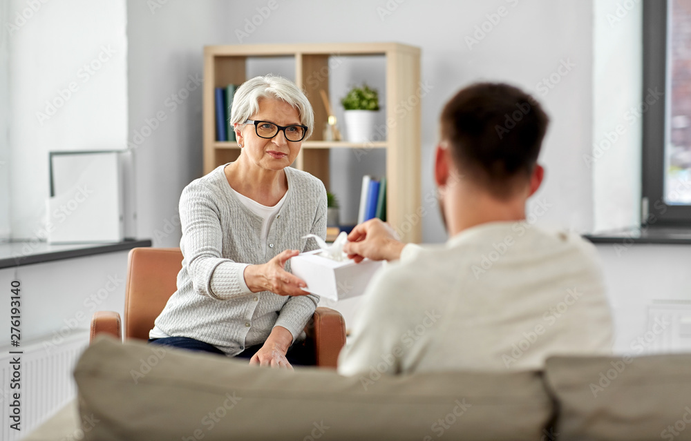 psychology, mental therapy and problem concept - senior woman psychologist giving tissues to sad young man patient at psychotherapy session psychology, mental therapy and problem concept - senior woman psychologist giving tissues to sad young man patient at psychotherapy session
