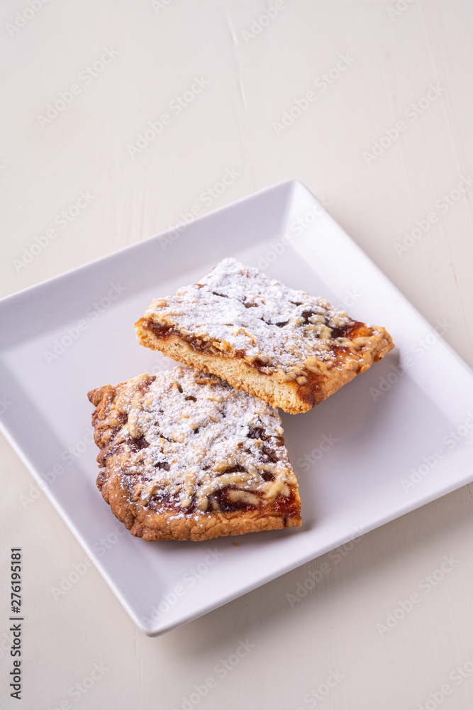 Two pieces of homemade cookies apricot jam powdered sugar in white square plate