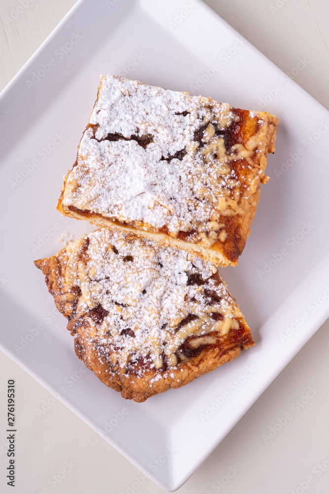 Two pieces of homemade cookies apricot jam powdered sugar in white square plate