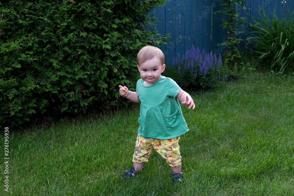 Horizontal full length view of cute fair toddler girl with cheeky expression learning to walk in lawn Horizontal full length view of cute fair toddler girl with cheeky expression learning to walk in lawn