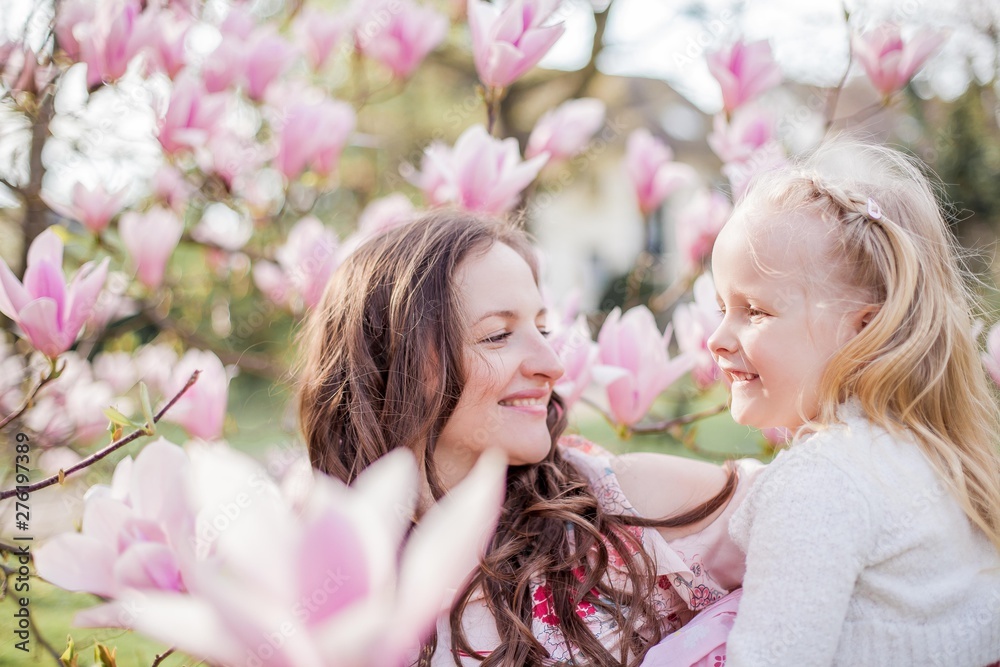 Fototapeta premium Beautiful young mother and little daughter near a blooming magnolia. Spring. Pink blooms.