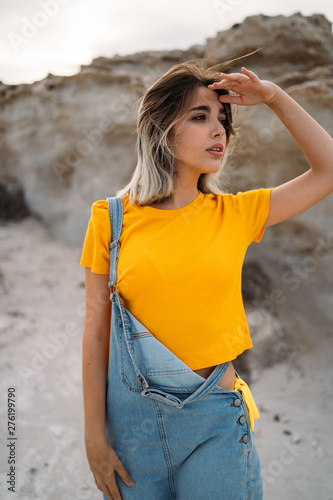 An attractive blonde young woman wearing yellow shirt at the beach near to stone cliff. Summer lifestyle fashion. © ManuPadilla