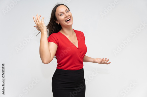 Portrait to the waist of a young pretty brunette woman of 30 years old in a bright red sweater with beautiful dark hair. Standing on a white background, talking, showing hands, with emotions