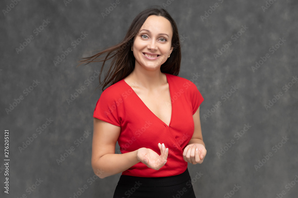 Portrait to the waist of a young pretty brunette woman of 30 years old in a bright red sweater with beautiful dark hair. It is standing on a gray background, talking, showing hands, with emotions Portrait to the waist of a young pretty brunette woman of 30 years old in a bright red sweater with beautiful dark hair. It is standing on a gray background, talking, showing hands, with emotions