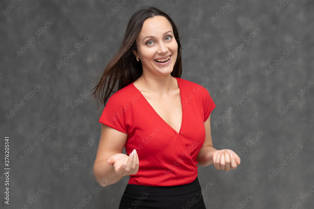 Portrait to the waist of a young pretty brunette woman of 30 years old in a bright red sweater with beautiful dark hair. It is standing on a gray background, talking, showing hands, with emotions Portrait to the waist of a young pretty brunette woman of 30 years old in a bright red sweater with beautiful dark hair. It is standing on a gray background, talking, showing hands, with emotions
