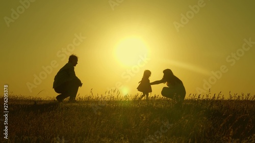 mom and dad play with their little daughter. happy child goes from father to mother. mother and Dad play with their daughter in sun. young family with child of 1 year. family happiness concept.