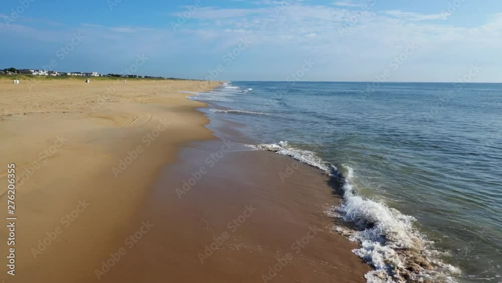 A 4k drone aerial view of a coastal beach in Virginia. flying forward seeing a birds-eye view of a bike and beachgoers walking along the beach with the waves crashing onto the sand. Water is turquoise A 4k drone aerial view of a coastal beach in Virginia. flying forward seeing a birds-eye view of a bike and beachgoers walking along the beach with the waves crashing onto the sand. Water is turquoise