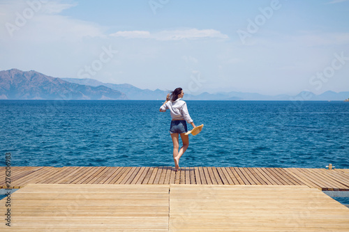 young sexy woman in a hat standing on the sea at the pier