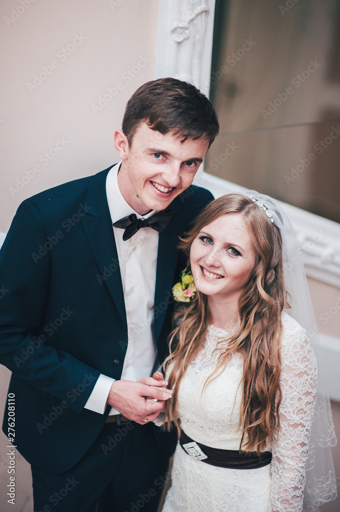 A stylish elegant bride and groom stands near the mirror. Look straight. Hold hands. hugs. Close up. Retro. Vintage architecture indoors. Portrait of newlyweds A stylish elegant bride and groom stands near the mirror. Look straight. Hold hands. hugs. Close up. Retro. Vintage architecture indoors. Portrait of newlyweds
