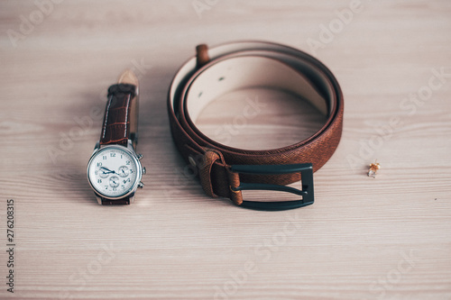 Wedding details, ideal groom accessories. .groom set with Belt, earring, Watches on wooden background. Concept of Men's fashion Accessories. Group of beautiful jewelry. Brown leather belt.