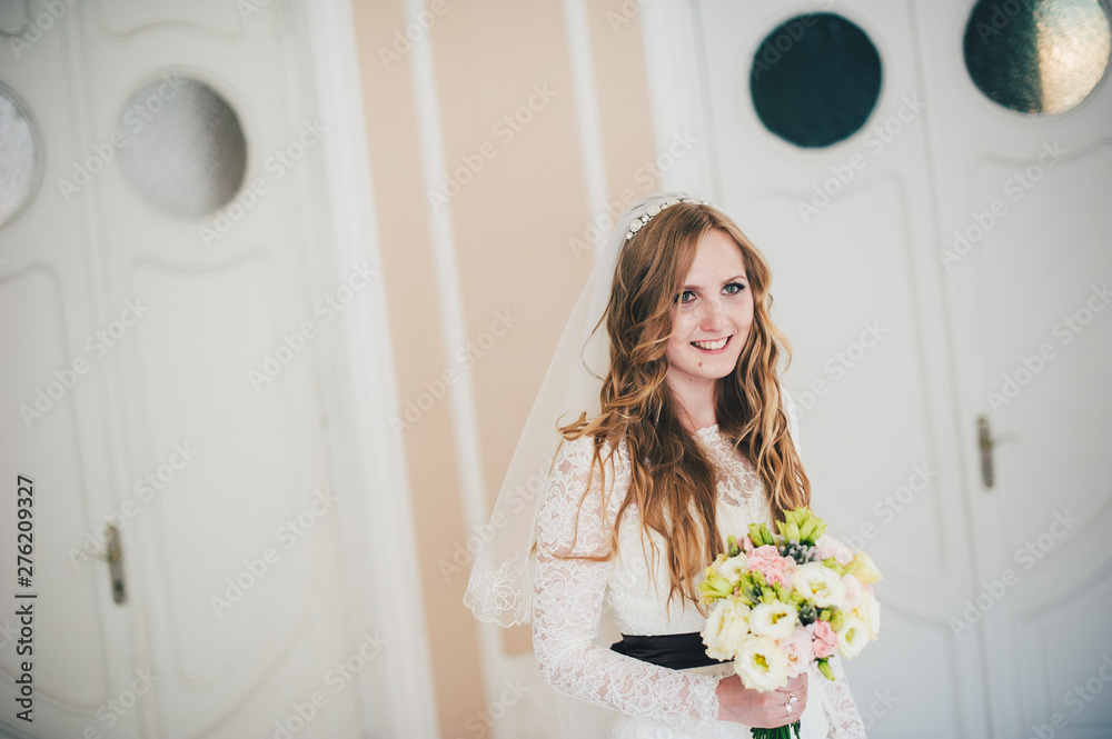 A stylish elegant bride with a bouquet of wedding flowers stand and poses. On the background of the wall and white doors. Close up. Portrait. Retro architecture indoors. Hotel. Number, room