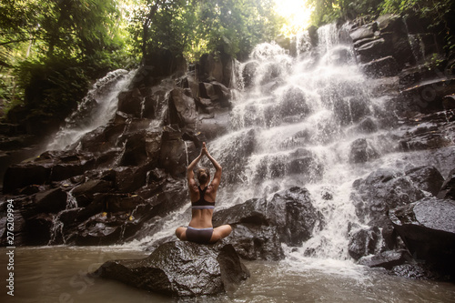Woman practices yoga near waterfall in Bali  Indonesia