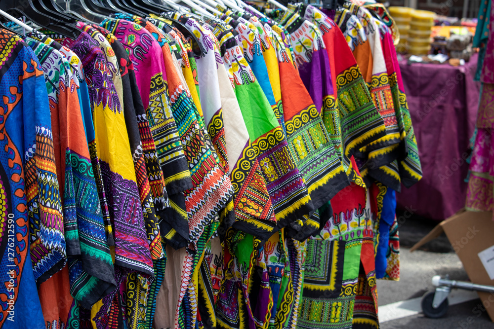 A rack of colorful dashikis displayed on hangers at an outdoor market.