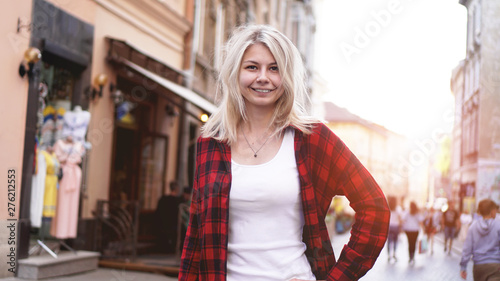 Lifestyle portrait of fashionable happy blonde with disheveled hair girl wearing a rock red shirt, white t-shirt having fun outdoors in the city © brillianata