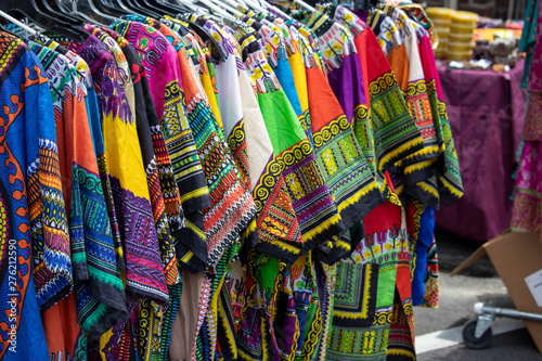 A rack of colorful dashikis displayed on hangers at an outdoor market.