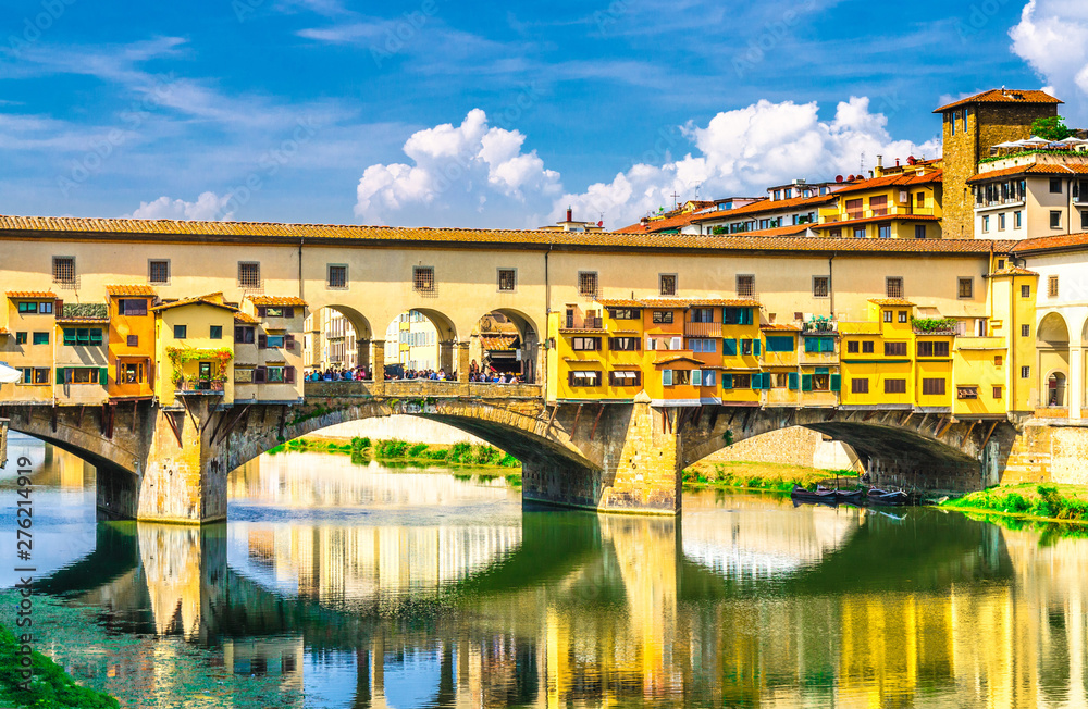 Ponte Vecchio stone bridge with colourful buildings houses over Arno River blue reflecting water in historical centre of Florence city, close up, blue sky white clouds, Tuscany, Italy