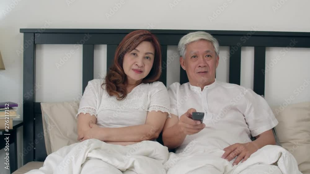 Asian elderly couple watching television in bedroom at home, Asia couple enjoy love moment while lying on the bed when relaxed at house. Enjoying time lifestyle senior family concept. Slow motion shot