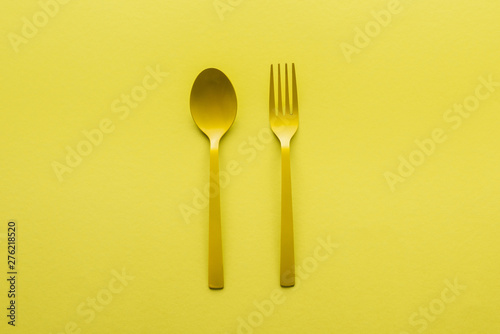 top view of yellow spoon and fork isolated on yellow