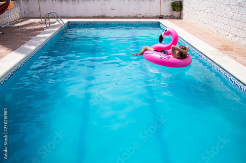 Young man floating in a inflatable flamingo in a blue pool a sunny day of summer vacation	