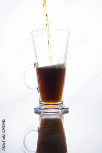 Dark beer is poured into a mug on a white background.