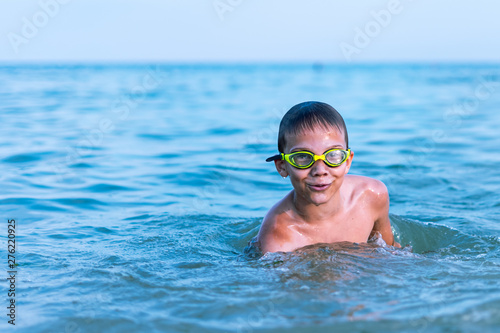 A 10-year-old boy swims in the sea at dawn with glasses for swimming.