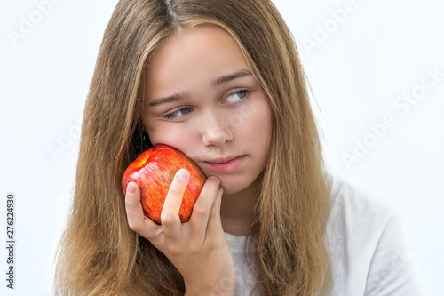 Portrait of upset dreaming young beautiful girl in white shirt , holding red apple in the hands near the cheek unhappy face on white background. Isolated ,copy space