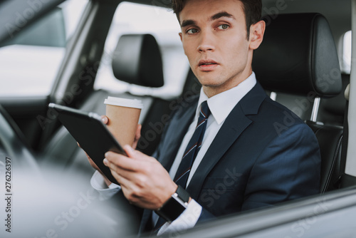 Handsome man in black suit holding hot drink in car