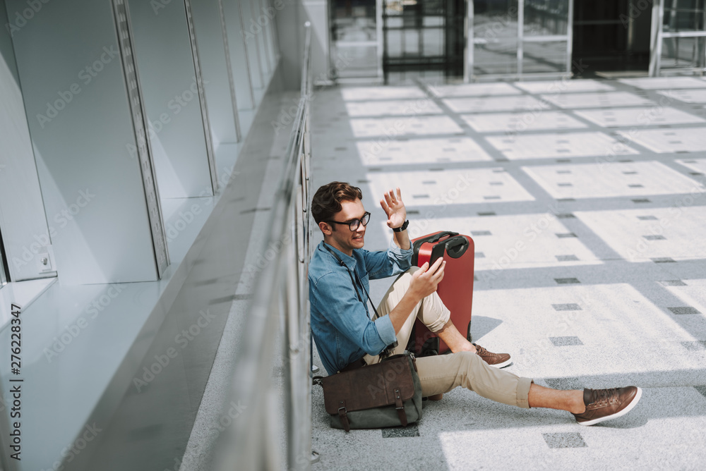 Happy young guy with mobile phone sitting in corridor in airport Happy young guy with mobile phone sitting in corridor in airport