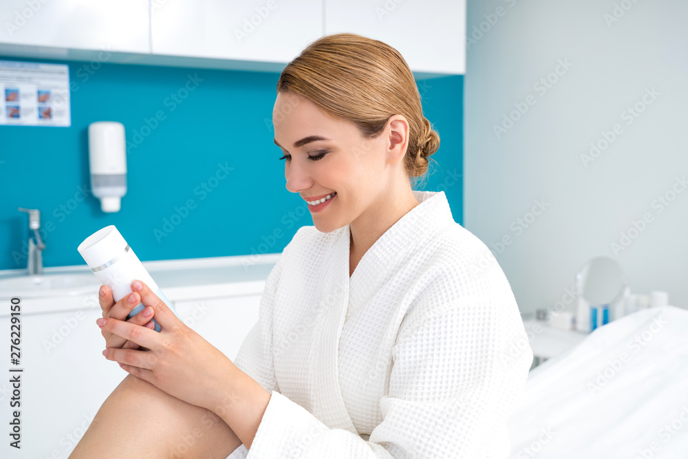 Smiling lady holding bottle of cream and looking at it Smiling lady holding bottle of cream and looking at it