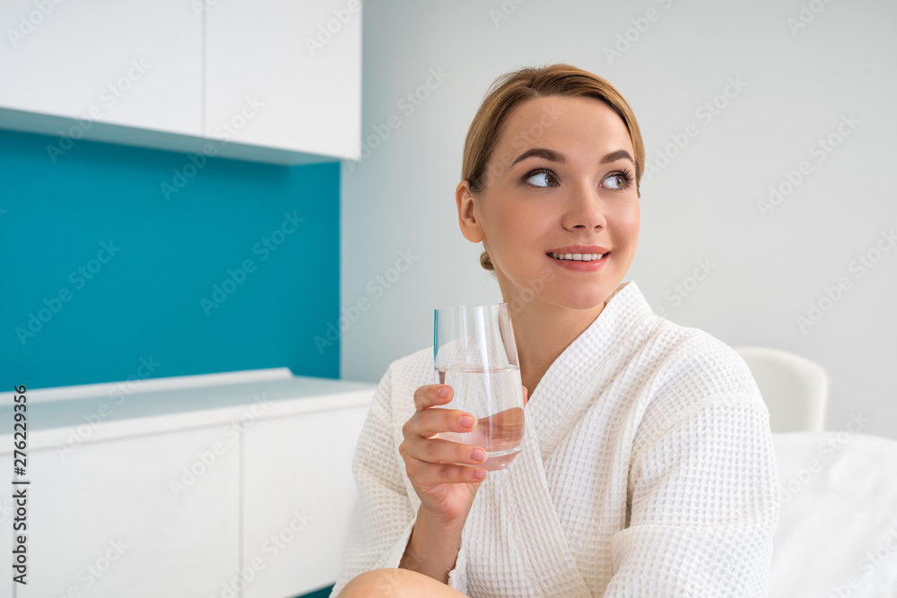 Cheerful lady looking away and holding glass of water Cheerful lady looking away and holding glass of water