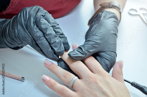 Manicurist in black gloves rubs varnished nail