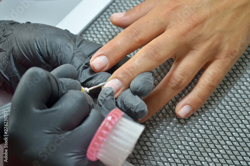 Master of manicure in black gloves and with a brush makes hardware manicure by nail cutter  top view