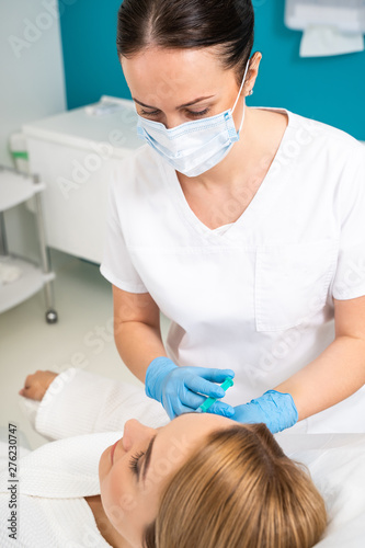 Waist up of female beautician making beauty procedures for client