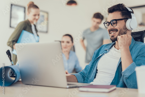 Smiling young man in headphones working with laptop in office