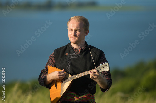 A man in traditional russian clothes playing balalaika on the field photo