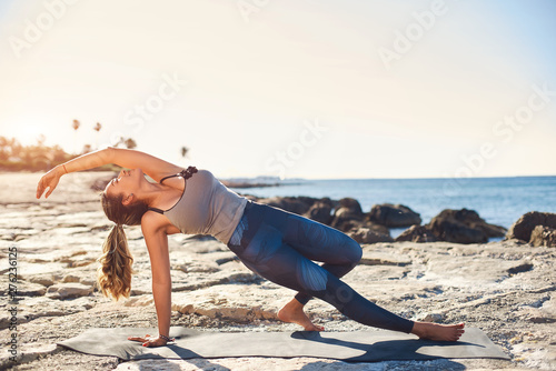 Young attractive woman practicing yoga on the beach at sunset.