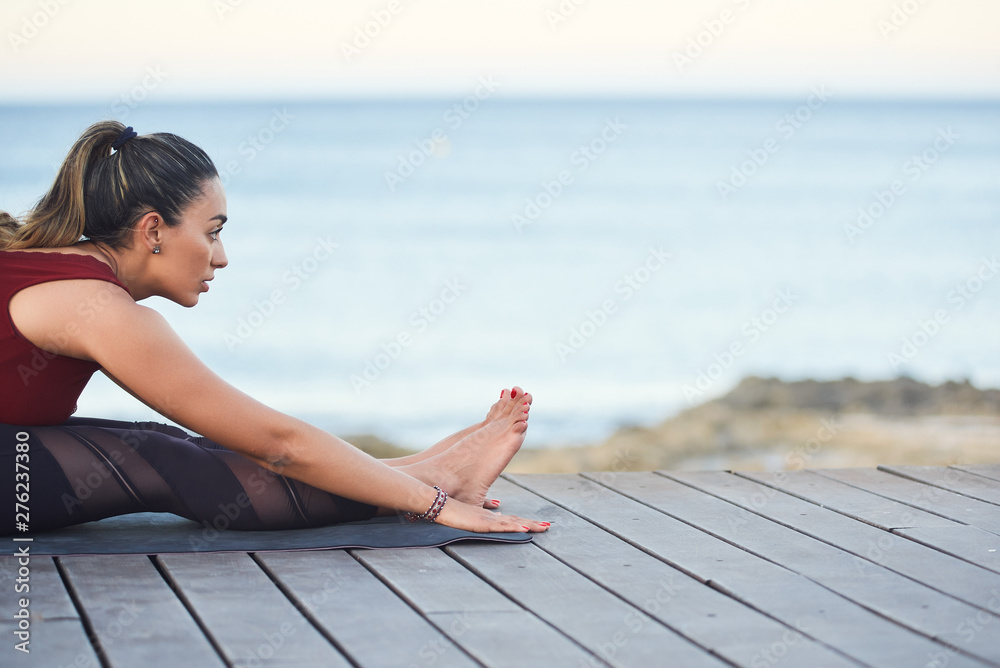 Young fit woman doing stretching exercises for legs against the sea.