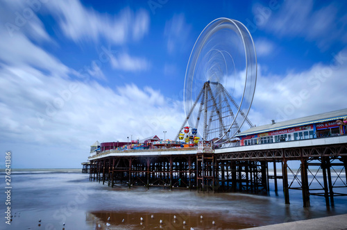 Wheel on the seaside Pier at Blackpool showing the wheel in motion with the sea partly out and seagulls on the water’s edge. 