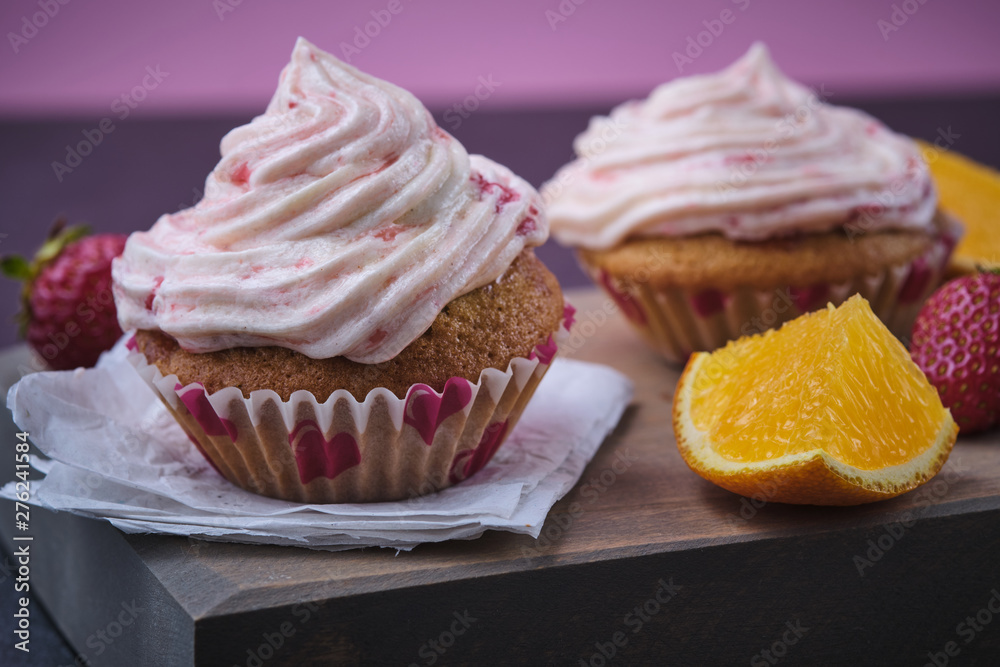 Orange cupcake with strawberry filling and butter cream with fresh berries. Dessert on a dark wooden board. Orange cupcake with strawberry filling and butter cream with fresh berries. Dessert on a dark wooden board.
