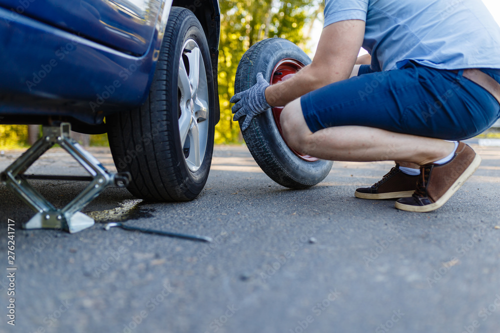 Mechanic in gloves lifts the car Jack on the side of the highway. Man is preparing to change the flat wheel lifting the car with a Jack on the side of the highway.