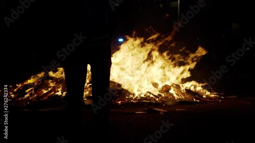 Dark silhouettes on the foreground and big fire on the background. People watching fire. Yellow flames rising up. Night of saint Joan in Barcelona. Fireworks and hot fire. 
