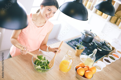 Smiling young woman mixing fresh salad in the kitchen.