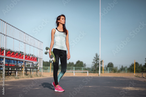 Teenager girl holding skateboard in hands on the cityscape background. Riding on scateboard. Summer concept of extreme sport. Close up portrait.