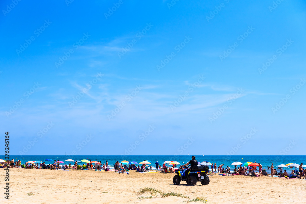 Valencia, Spain - June 23, 2019: Police in quad patrolling a beach full of tourists and holiday makers to avoid thefts and thefts typical of the summer time.
