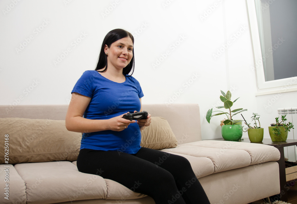Pregnant girl playing video games , sitting on couch Pregnant girl playing video games , sitting on couch
